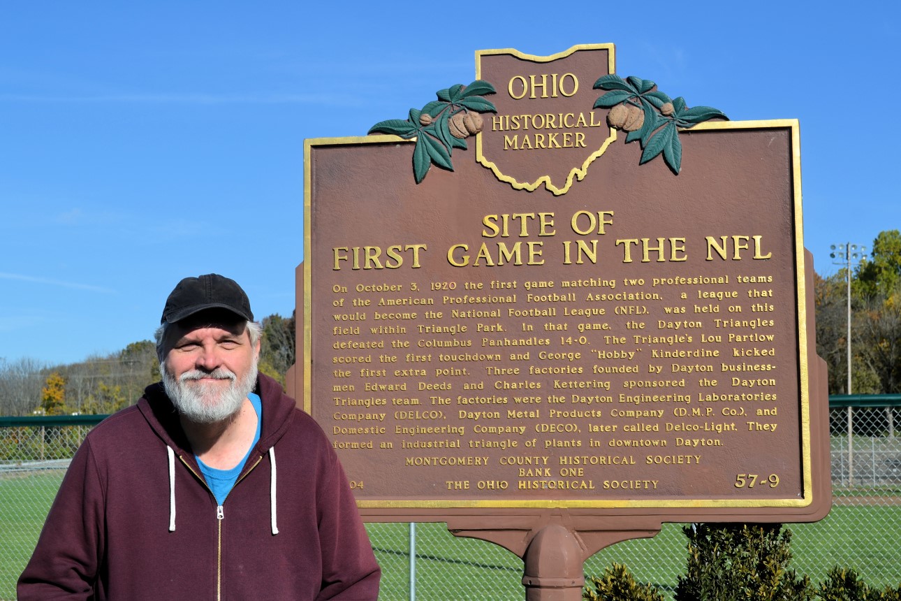 Bruce standing beside NFL first game historical marker